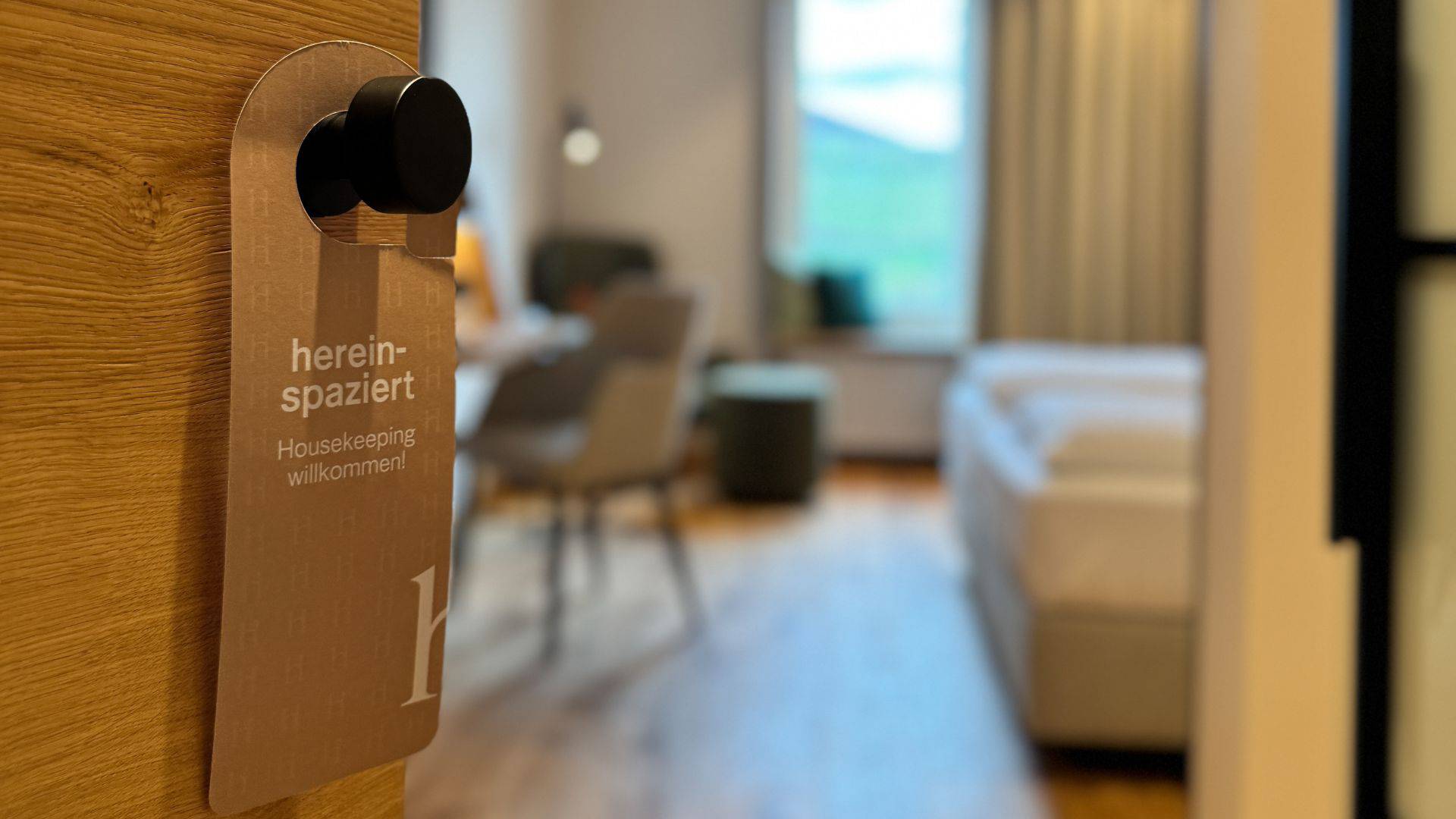 Türanhänger „bitte nicht stören“ vor unscharfem Blick in ein Zimmer mit Bett und Sitzbereich.